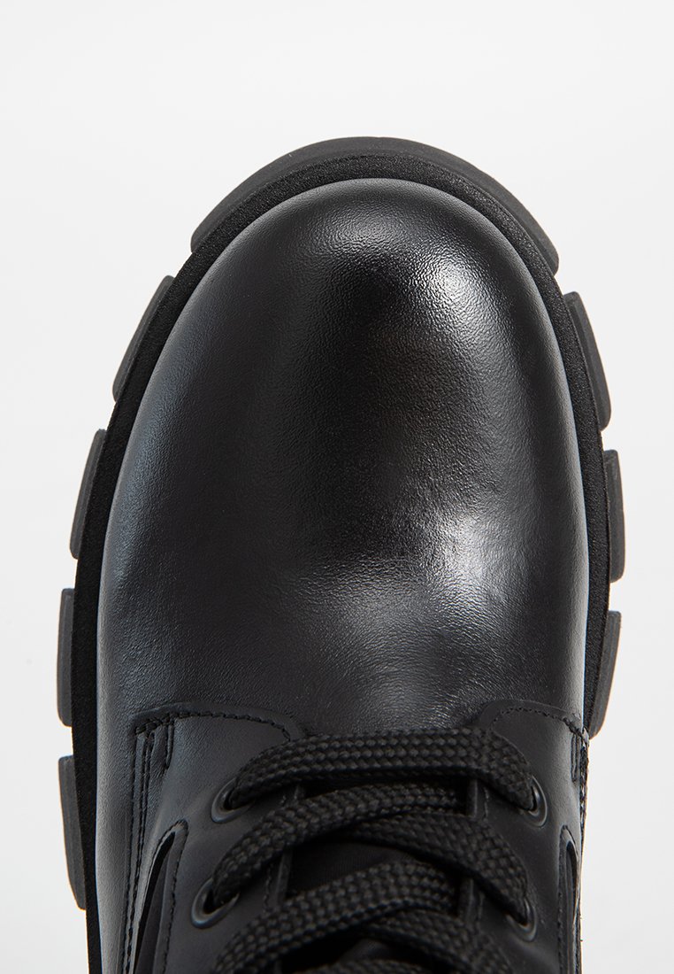 Bota de cuero negro con punta redondeada, parte superior texturizada y suela de goma gruesa. Presenta cordones negros y corte lateral para ventilación.