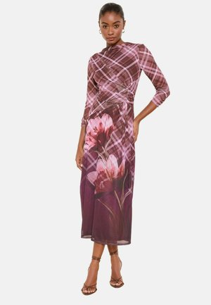 Žena v dlhých rukávoch a šatách dlhých až po členky, s vrškom v ružovo-hnedú károvanú vzoru a veľkým ružovým kvetinovým vzorom na tmavofialovej sukni.