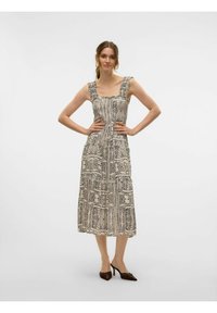 Midi-jurk met een zwart-wit tribalprint, voorzien van brede bandjes, een geraffineerde halslijn en een gelaagde rok; gecombineerd met bruine hakken.