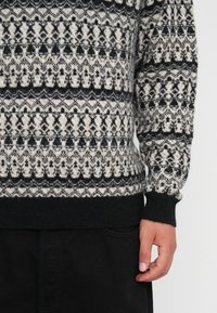 Μαύρο και κρέμα πλεγμένο πουλόβερ με γεωμετρικά σχέδια, με ριχτές μανσέτες και στρίφωμα, φτιαγμένο από υφασμάτινη υφή, με κοντή εφαρμογή.