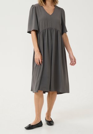 Szara sukienka z dekoltem w serek, krótkimi bufkowatymi rękawami, marszczoną talią i długością do kolan. Do tego czarne płaskie buty. Gładka faktura.