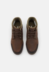 Botas de cuero marrón con un diseño de cordones, cuello acolchado verde y suela de goma negra. La parte superior texturizada y el logo grabado presentan detalles destacados.