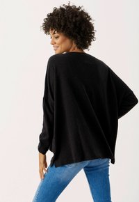 Übergroßer schwarzer Pullover aus weichem Strick mit einer lockeren Passform, weiten Ärmeln und einem asymmetrischen Saum, kombiniert mit eng anliegenden blauen Jeans.