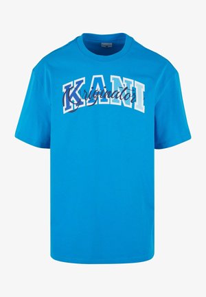Camiseta de algodón azul con mangas cortas, que presenta un gran texto en blanco y azul que dice "KANI" y cursiva "originator" debajo. Diseño simple de cuello redondo.