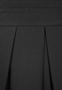 Gros plan d'une jupe en tissu noir avec une large ceinture et deux plis devant.