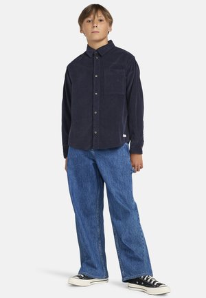 Camicia di cotone a coste blu navy con taschino, abbinata a jeans in denim blu a vita alta e sneakers in tela nere.
