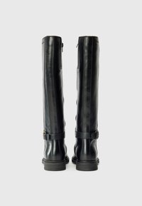 Bottes en cuir noir montantes jusqu'aux genoux avec une texture lisse, des boucles en argent et un petit talon carré ; comportent une fermeture éclair à l'arrière et des détails cousus.