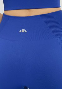 Niebieskie legginsy sportowe z fakturowanymi panelami i dopasowanym krojem. Posiadają małe logo w kolorze szarym na pasie i gładkie wykończenie.