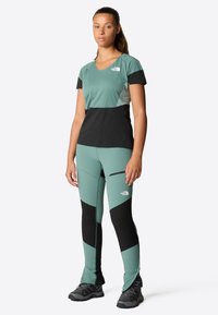 Miętowa bluzka sportowa z czarnymi akcentami, w zestawie z dopasowanymi legginsami w miętowym kolorze z czarnymi detalami. Charakteryzuje się dopasowanym krojem i teksturowanym materiałem.