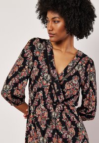 Czarna sukienka z kolorowym wzorem w kwiatowy paisley, dekoltem w serek i puffowanymi rękawami, z wcięciem w talii i lejącym materiałem.