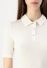 Kremfarget polo-skjorte med korte ermer, med en klassisk krage og tre knapper, laget av et glatt, lett stoff.