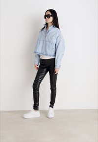 Lichtblauwe cropped denimjas met een hoge kraag, gecombineerd met strakke zwarte leren broeken en witte sneakers. Minimalistisch ontwerp en een zachte textuur.