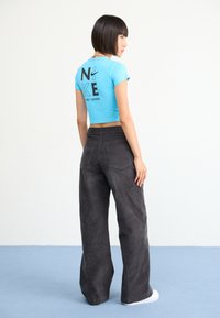 Blue cropped t-shirt with black text and logo on the back, paired with high-waisted, loose-fitting, dark gray pants.