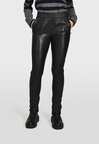 Pantaloni in ecopelle nera con una vestibilità slim, cintura elastica e tasche laterali. Superficie testurizzata con una finitura liscia, abbinati a stivali neri chunky.