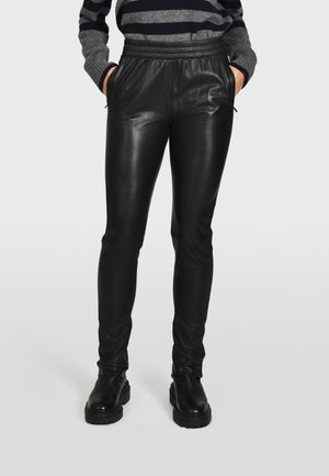 Sorte faux læderbukser med slim fit, elastisk talje og sidelommer. Tekstureret overflade med en glat finish, parret med chunky sorte støvler.