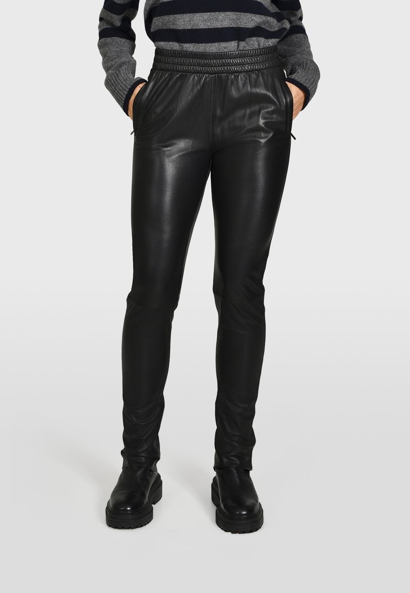 Pantaloni in ecopelle nera con una vestibilità slim, cintura elastica e tasche laterali. Superficie testurizzata con una finitura liscia, abbinati a stivali neri chunky.