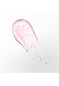 Tache de gel clair avec de petites perles roses étalées sur fond blanc, montrant la texture et la consistance d'un produit cosmétique ou de soin de la peau.
