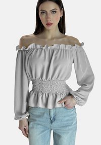 Top grigio senza spalline con colletto a volant, vita arricciata e maniche lunghe. Abbinato a jeans in denim chiaro.