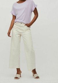 Svetle fialový top s krátkým rukávem a volánkovými okraji, spárován s krémovými širokými kalhotami a béžovými sandály na podpatku, vykazuje pohodlný střih.