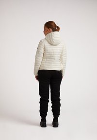 Giacca a vento bianca con cappuccio, texture a coste e cuciture orizzontali, abbinata a pantaloni neri a sigaretta e scarpe nere.