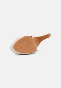Chaussure à talon haut beige vue par le dessous, présentant une semelle à motifs floraux et en spirale.