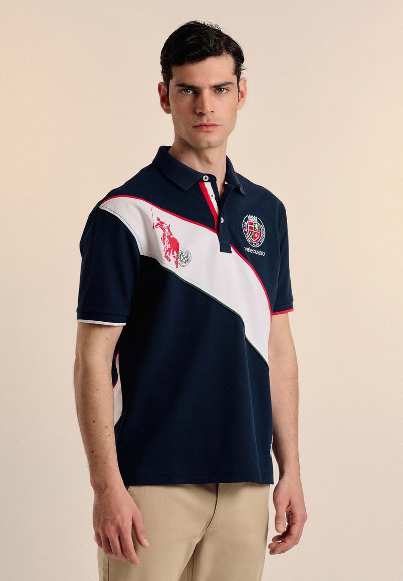 Polo de color marino con rayas diagonales blancas, acentos rojos y logo bordado. Presenta un cuello tipo polo y mangas cortas. Material mezcla de algodón.
