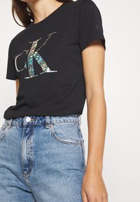 Czarny bawełniany t-shirt z odblaskowym logo "CK". Połączony z jeansami o wysokim stanie w jasnoniebieskim kolorze. Krótkie rękawy i luźny krój.