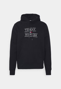 Czarna bluza z kapturem i kieszenią z przodu, z białym napisem: "TOMMY HILFIGER" oraz małym logo w kolorach czerwonym i niebieskim. Miękki materiał, regulowany kaptur, ściągacze przy mankietach.