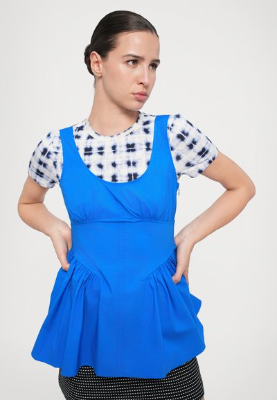 Blue sleeveless top with a fitted bodice and pleated hem, layered over a white and navy tie-dye shirt with short sleeves.