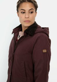 Burgunderfarbene Jacke mit einem Cordkragen, Reißverschluss, Seitentaschen und Lederlogo-Patch, entworfen für die Freizeit. Mit Kapuze.