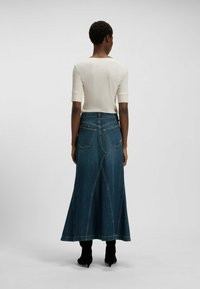 Pitkä farkkuhame tummansinisenä, helma levenee ja näkyvissä ovat sauman yksityiskohdat, yhdistetty vaalean sävyiseen istuvaan toppiin. Mustat nilkkurit.