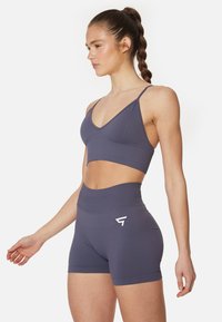 Šedý športový crop top a šortky so zvýšeným pásom vyrobené z elastického materiálu, s minimálnymi švami a malým bielym logom na šortkách.