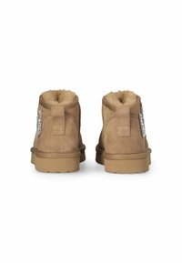 Botas de tobillo de ante marrón con forro de felpa sintética, tira trasera para facilitar el calce y adornos de strass decorativos en el costado. Suela de goma para mayor tracción.