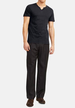 Schwarzes T-Shirt mit kurzen Ärmeln, V-Ausschnitt und Knopfdetails, kombiniert mit schwarzen Anzughosen und braunen Schuhen.