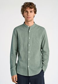 Camisa verde de botones con cuello mao, mangas largas y bolsillo en el pecho. Textura ligera con botones en contraste. Corte informal.