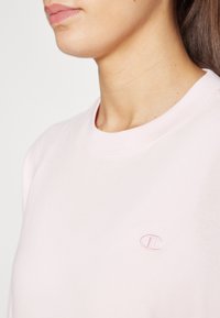 Lyserosa bomull t-skjorte med ribbet rund hals. Har en liten brodert logo på venstre brystområde. Glatt tekstur.