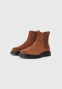 Cizme ankle din suede maro, cu panouri laterale elastice și vârf rotund, având o talpă din cauciuc negru, conturată, pentru o aderență suplimentară.