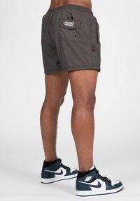 Donkergrijze zwemshorts met een elastische tailleband, een achterzak en logodetail; gecombineerd met zwart-witte hoge sneakers.