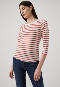 Maglietta a maniche lunghe a righe rosse e bianche con scollo rotondo e un piccolo logo. Abbinate a jeans di denim blu scuro.