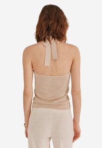Beige Haltertop mit glänzender Textur, rippendesign und langen Bindebändern im Rücken, kombiniert mit hellen Hosen.