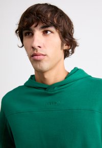 Green fleece hoodie with a front pocket, drawstring hood, and embroidered logo on the chest. Features a smooth texture and relaxed fit.