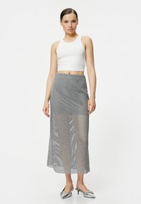 Sølvnet stof nederdel med et langt, flydende design; har et geometrisk diamantmønster og en tætsiddende talje, parret med en hvid cropped top.
