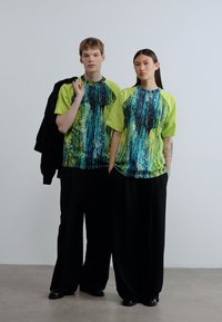 Δύο άτομα φορούν ταιριαστά πολύχρωμα πράσινα και μπλε μπλουζάκια με μαύρο, άνετο παντελόνι. Τα μπλουζάκια έχουν μανίκια raglan.