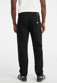 Melni džinsa bikses ar taisnu kāju dizainu, ar aizmugurējām kabatām un nelielu trīsstūra logotipu pie jostasvietas. Teksturēta auduma, minimāla apdare.