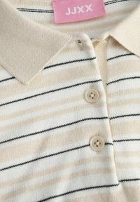 Polo rayé beige et blanc avec des lignes noires. Comprend un col côtelé, trois boutons, et une étiquette rose avec le texte "JJXX".