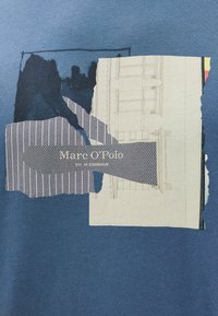 Tecido azul com remendos de tecido em camadas, apresentando um design listrado e um esboço arquitetónico impresso, incluindo o rótulo "Marc O'Polo".
