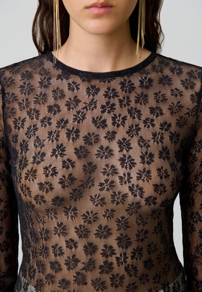Top in pizzo nero con un motivo floreale, maniche lunghe, scollo rotondo e finitura testurizzata. Accentuato con orecchini a goccia dorati.