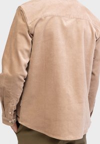 Brązowa koszula sztruksowa o prostym kroju, z przeszyciem na karku, mankietami zapinanymi na guziki i miękkim, teksturowanym wykończeniem.