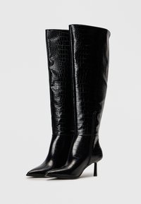 Schwarze knöchelhohe Stiefel aus glänzendem, krokodilgeprägtem Leder. Spitz zulaufende Zehen, schmaler Absatz und ein dezentes Reißverschlussdetail an der Seite.
