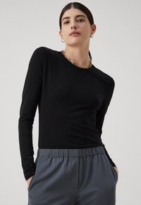 Čierny top s dlhým rukávom, priliehavého strihu, hladkej textúry a okrúhlym výstrihom, skombinovaný so šedými nohavicami s elastickým pásom.